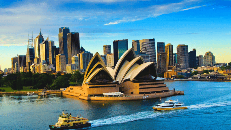 The iconic Sydney Opera House and city skyline on a bright sunny day, with ferries on the harbour, representing a top destination for British expats moving to Australia.