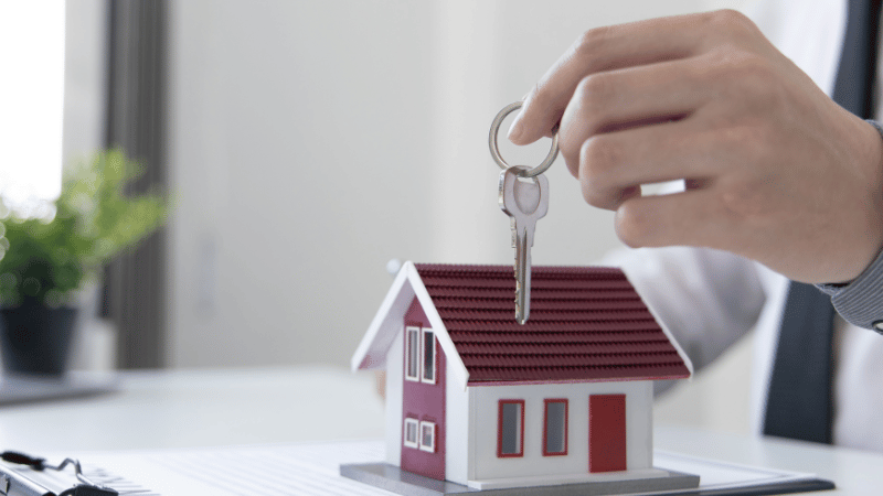 A professional mortgage broker's hand holding a set of keys over a model house, symbolizing the release of equity from a buy-to-let property.